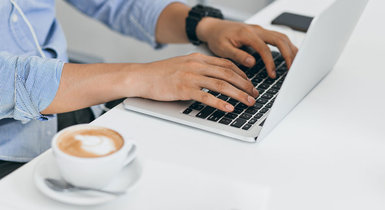 Person schreibt Bewerbung am Laptop mit Tasse Kaffee